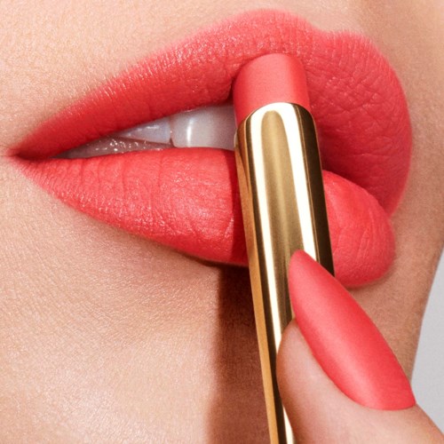 A person applies pink lipstick to lips with a tube, lips slightly parted showing teeth, skin is smooth.