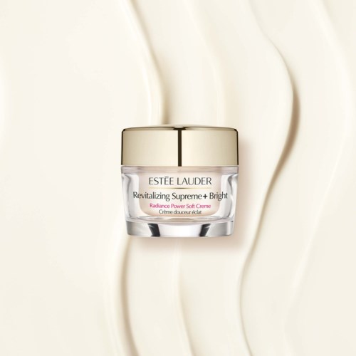 Een potje met Estee Lauder huidverzorgingscrème met een gouden deksel op een golvende lichtgekleurde achtergrond.