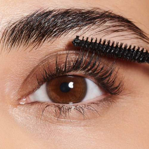 Een persoon brengt mascara aan op gekrulde wimpers met een kwast, oog open, bruine ogen, natuurlijke make-up uitstraling.