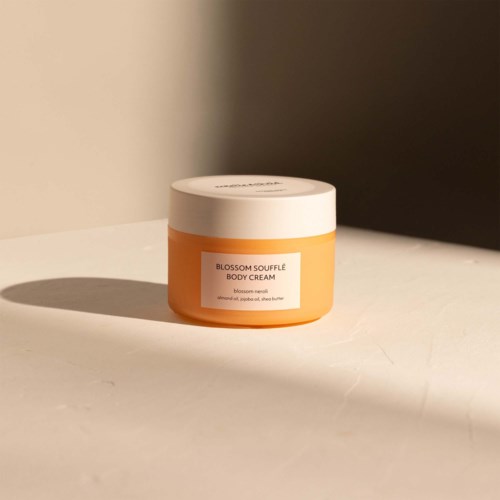 Een kleine pot Blossom Soufflé Body Cream met witte deksel en oranje container. Het staat op een witte ondergrond.
