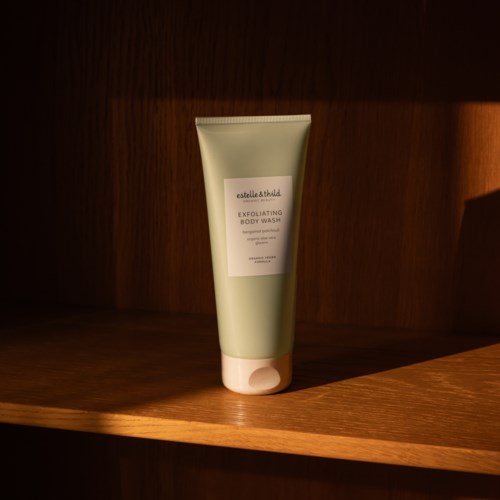 Een lichtgroene tube met exfoliërende lichaamswas op een houten plank met warm licht.