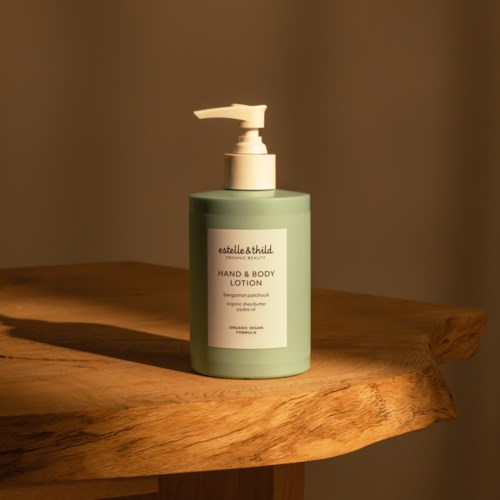 Groene lotionfles met pomp op houten oppervlak, etiket zegt 'Estelle & Thild Hand & Body Lotion.'