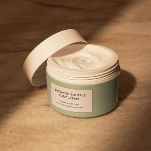 Een pot Bergamot Souffle Body Cream met open deksel, met de gladde creme binnenin.
