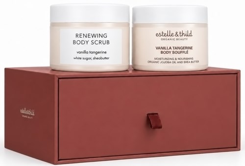 Två burkar med kroppsskrubb och kroppssoufflé på en röd låda, etiketter med doft av vanilj och mandarin. "Renewing Body Scrub" och "Estelle & Thild."