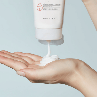 Iemand brengt witte crème aan op de hand van een ander persoon uit een tube, met een eenvoudige lichte achtergrond.