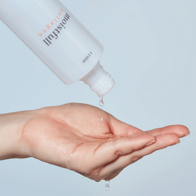Een hand met een druppel vloeistof, een fles die vloeistof giet, op een lichtblauwe achtergrond.