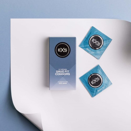 Eine Schachtel vegane snug fit Kondome und zwei Kondomverpackungen auf einer weißen und blauen Oberfläche.