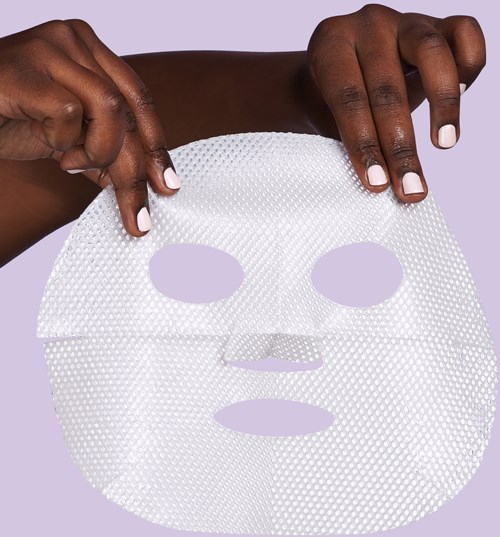 Två händer håller ett vitt ansiktsmask mot en lavendelfärgad bakgrund.