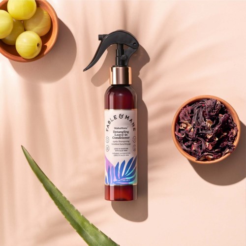 En brunspraydunk med svart pump och vit etikett omgiven av gula druvor och torkade lila blommor.