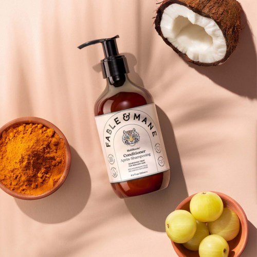 En brunt tvålflaska märkt Fabulous Conditioner omgiven av gurkmejapulver, gröna äpplen och en halverad kokosnöt.