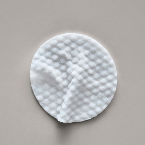 Een ronde witte wattenschijf met gestructureerd oppervlak op een lichtgrijze achtergrond.