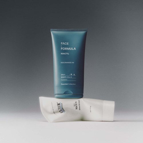 Two tubes of skincare products, one blue and one white, stand on a gray surface with a plain gray background.
