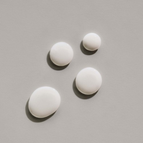 Four white pills of different sizes on a light gray background.