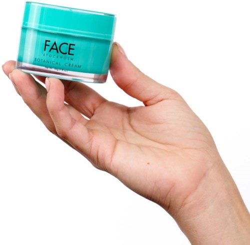 Een hand houdt een kleine turquoise pot met 'FACE' en 'BOTANICAL CREAM'.