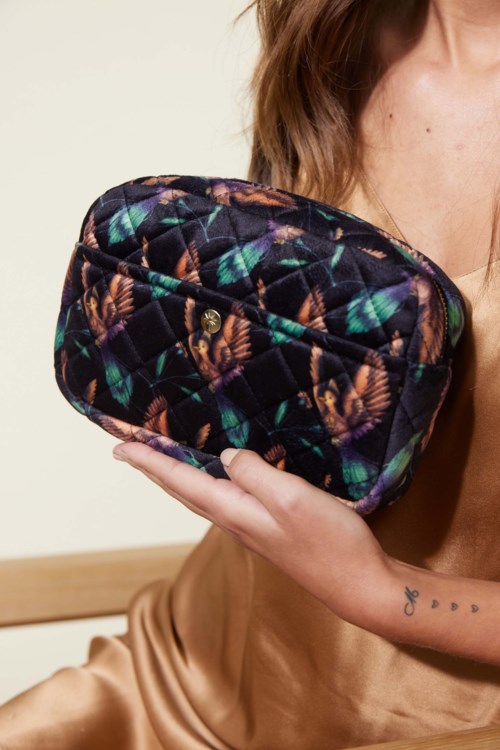 A woman holds a quilted bag with a colorful, leafy pattern.