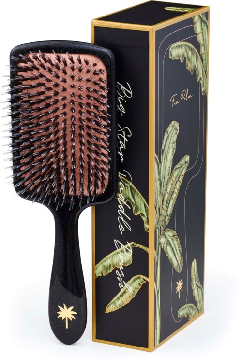 A black hairbrush with pink bristles and a palm tree design on the handle, next to a black box with green leaves.