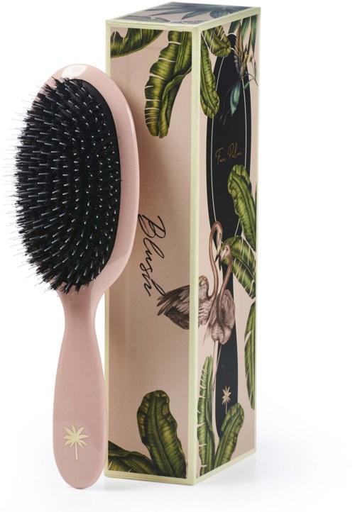 A pink hairbrush with black bristles next to a balcony-themed box with green leaves and flamingos.