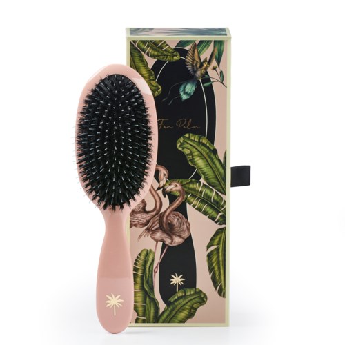 A pink hairbrush with black bristles stands next to decorative box with jungle leaves and animals design.