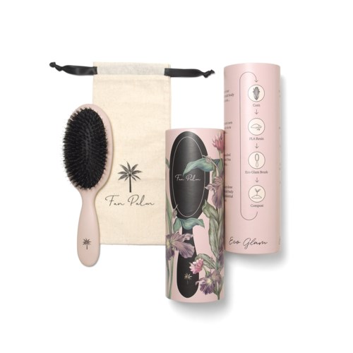 A wooden brush with black bristles, a beige pouch, and two pink cylindrical containers with floral and informational designs.
