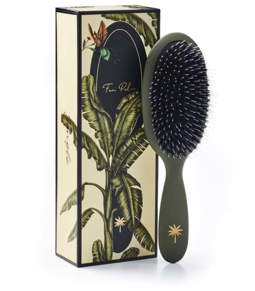 A hairbrush with a green handle and black bristles, standing next to a tall, decorative box with tropical leaf design.