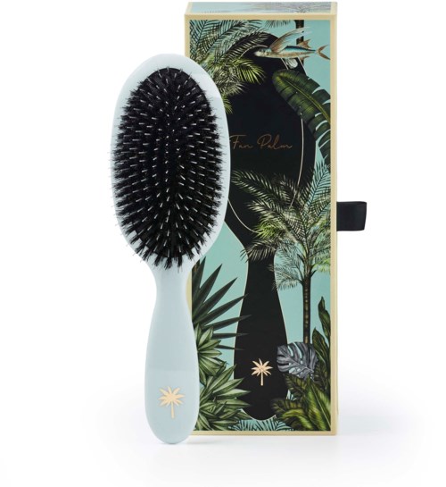 A hairbrush with a white handle and black bristles, next to a colorful tropical-themed box.