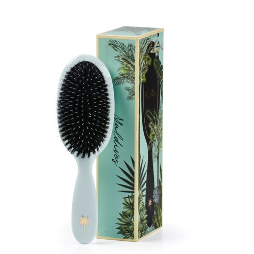 A hairbrush with a white handle and black bristles. It is next to a decorative box with palm trees and tropical plants.