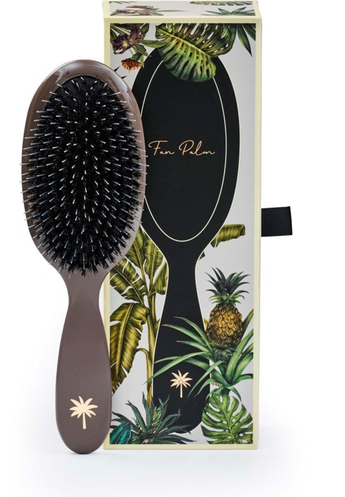 A hairbrush with black bristles in front of a tropical-themed box with pineapple and leafy designs.