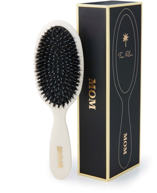 A hair brush with black bristles and a white handle, next to a black and gold box. The box has "MOM" written on it.