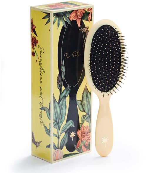 A hairbrush with a floral design and a black cushioned base, next to a colorful box with plants and flowers.