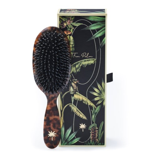 A hairbrush with a tortoiseshell handle and black bristles, placed in front of a floral and animal print box.
