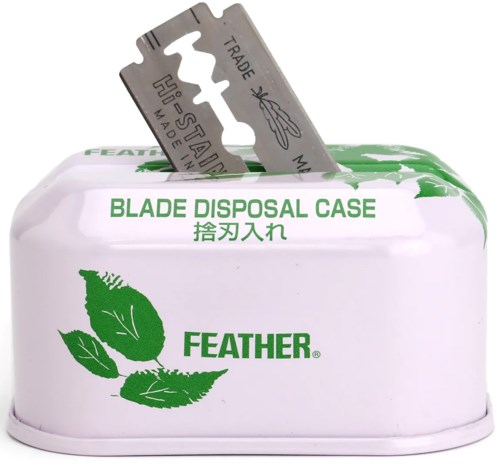 Een witte container met een opening voor scheermesjes, groene bladeren en tekst. Bevat een klein scheermesje.