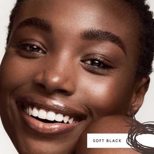 A smiling woman with dark skin, showing white teeth, close-up of her face with natural makeup and textured hair.