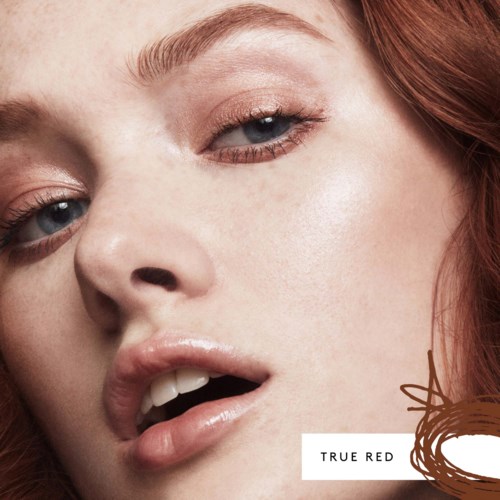 Close-up of a woman with red hair, light skin, and a subtle, natural makeup look. She appears to be leaning or looking slightly.