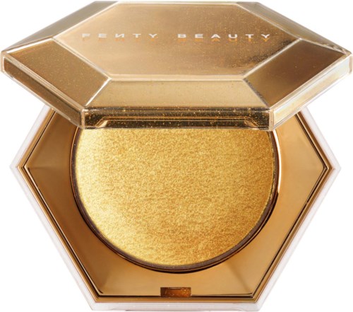 A golden, shiny makeup product in a hexagonal compact with a transparent, gold-tinted lid. The brand name is on top.