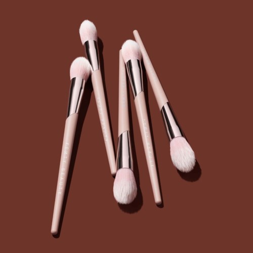 Set of five pink makeup brushes with white bristles on a brown background.