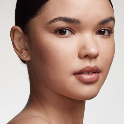 A young woman with clear skin, dark hair pulled back, and wearing small earrings, looking softly at the camera.