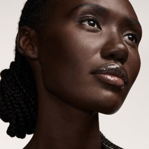 A close-up of a woman with dark skin, braided hair, and shiny lips looking thoughtfully.