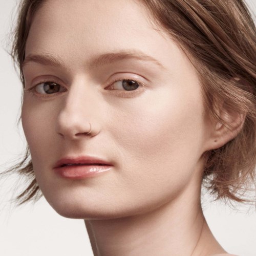 A young woman with short brown hair, light skin, and a nose ring. She has a neutral expression and natural makeup.