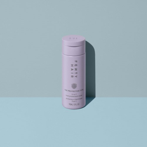 A pink bottle of Fenty Hair product stands upright on a light blue surface with a shadow behind it.