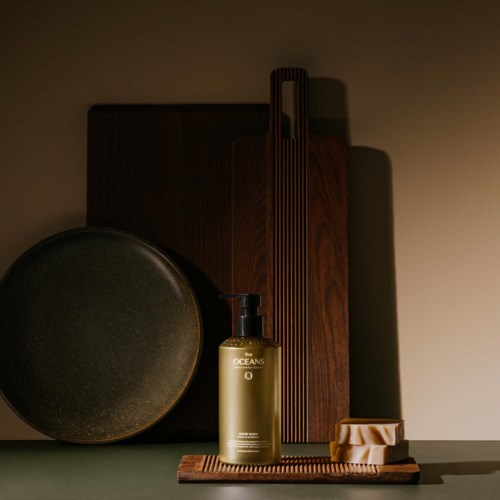 A black round plate, a golden bottle labeled 'OCEANS', a striped wooden object, a soap with a dish, and a wooden tray.