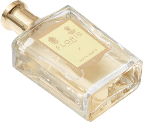 Een doorzichtige glazen parfumfles met een gouden dop, gelabeld 'FLORES' en 'EAU DE TOILETTE'.