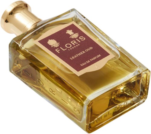Eine goldfarbene Parfümflasche liegt auf der Seite mit einem braunen Etikett, auf dem 'Floris London Leather Oud Eau de Parfum' steht.