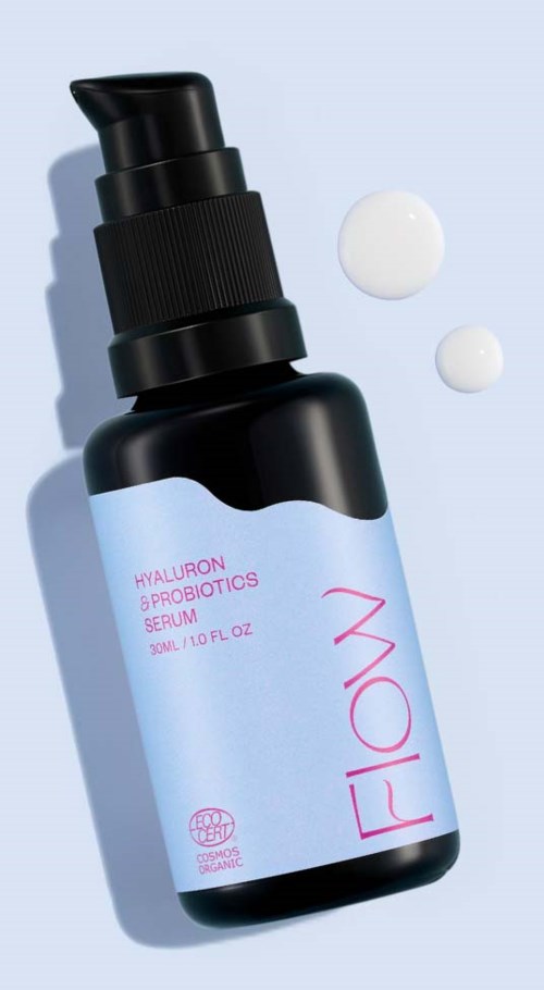 Een zwarte fles met een pomp en label 'FLOW' en 'Hyaluron & Probiotics Serum,' met twee dollops crème ernaast.