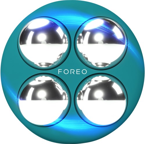 Een teal ronde apparaat met vier glanzende zilveren ballen en het woord "FOREO" in het midden.