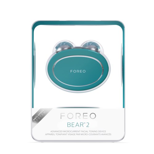 Een turquoise gezichtsapparaat in een doos met 'FOREO BEAR 2' voor huidverstrakking en schokbestendigheid. Het heeft twee ronde delen.