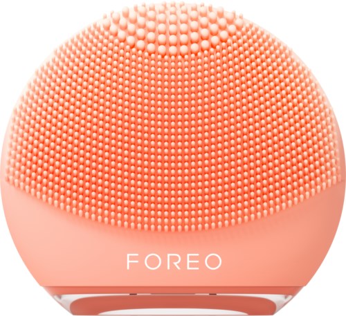 Een ronde, oranje gezichtsreinigingsapparaat met kleine borstelharen, onderaan met 'FOREO' geschreven.
