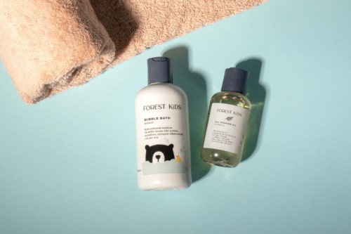 Two Forest Kids bottles, one with a bear design, placed on a light blue surface with a brown towel nearby.