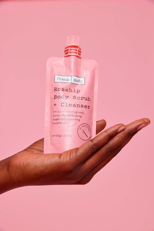 Een hand houdt een roze tube lichaamscrème en cleanser op een roze achtergrond.