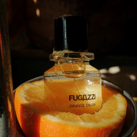 Ein Parfümflasche mit dem Label 'FUGDZZI ORANGE CRUSH' liegt in einer halben Orange.
