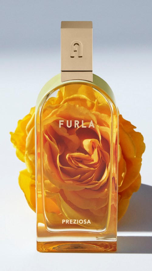 En parfymflaska med gula blommor inuti, märkt 'Furla Preziosa'. Flaskan har ett krämfärgat lock och en böjd form.
